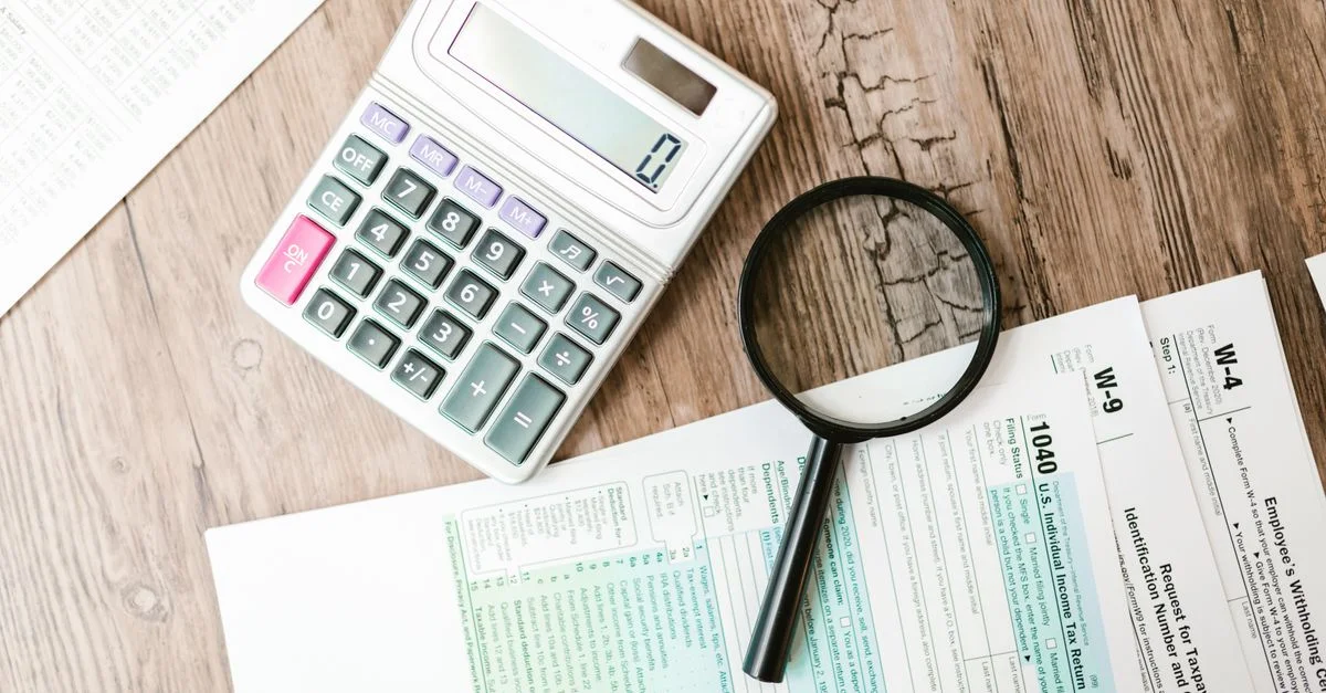 Des formulaires fiscaux disposés avec une calculatrice et une loupe sur une surface en bois, parfaits pour des thèmes financiers.
