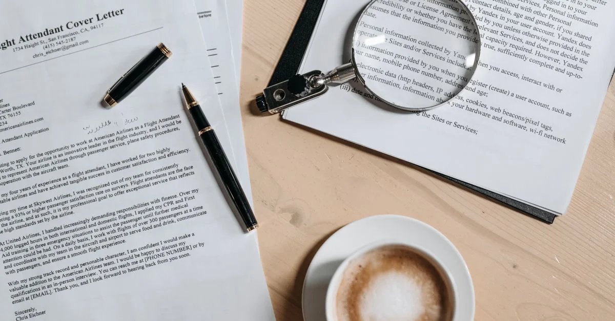 Une vue de dessus de café et de documents de candidature avec une loupe sur un bureau en bois.