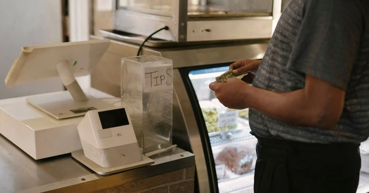Gros plan d'une personne effectuant un paiement en espèces au comptoir d'un magasin avec une caisse enregistreuse numérique.