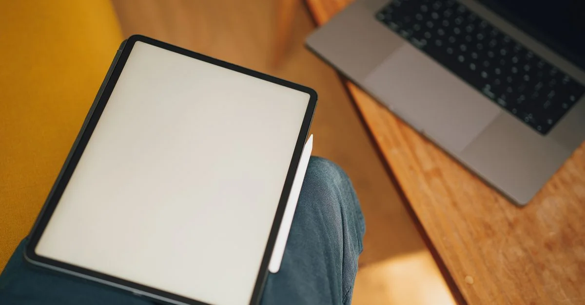 Une tablette numérique sur les genoux à côté d'un ordinateur portable sur une table en bois, idéale pour travailler ou étudier.