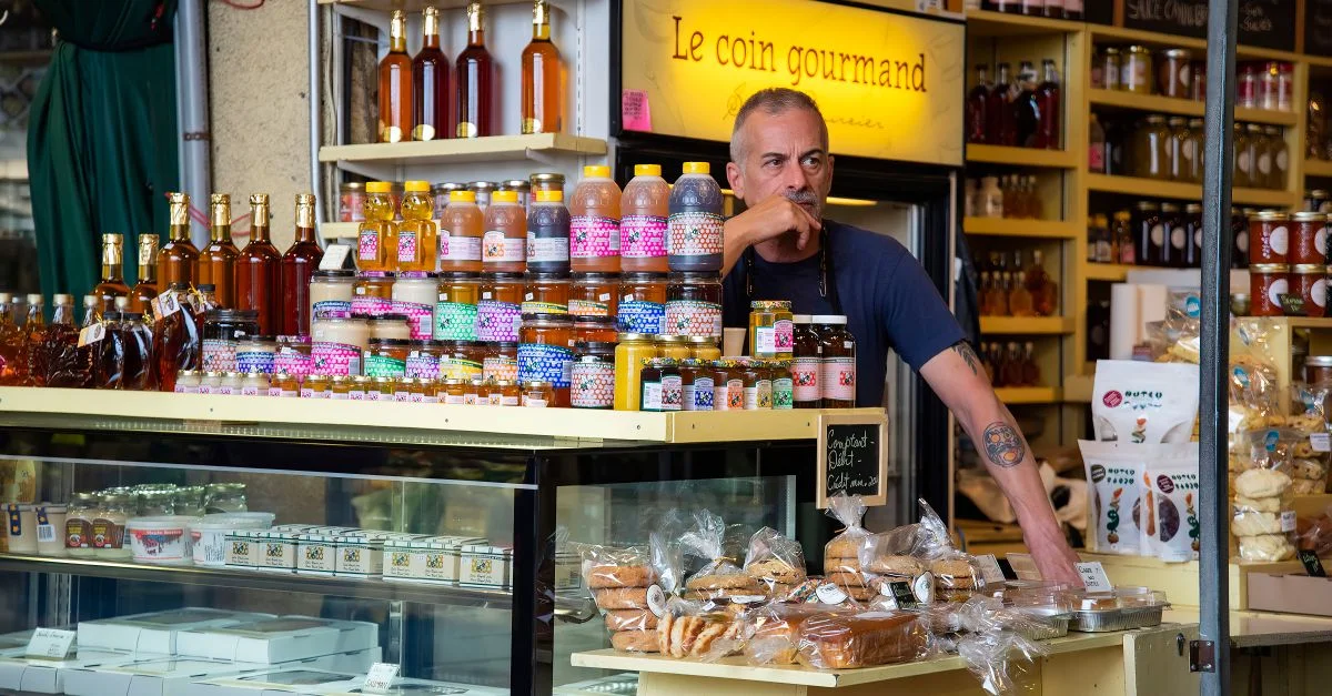 Un stand de marché coloré présentant une variété de produits gastronomiques avec un commerçant attentif.