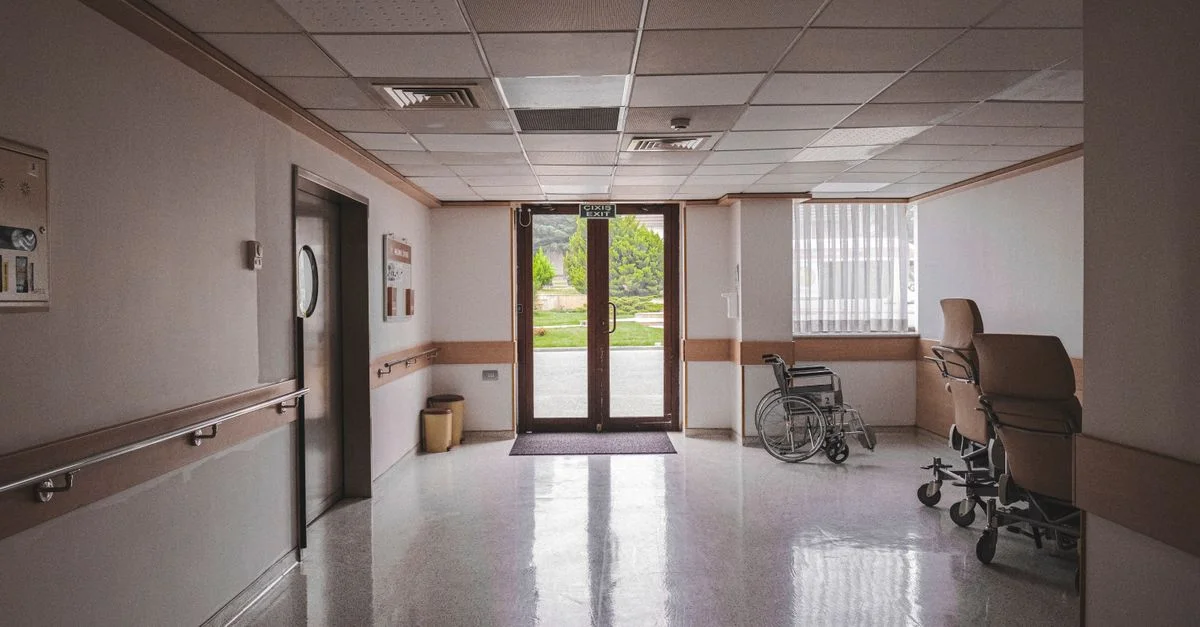 Couloir d'hôpital avec fauteuil roulant, portes vitrées réfléchissantes et vue extérieure. Idéal pour les thèmes de la santé.