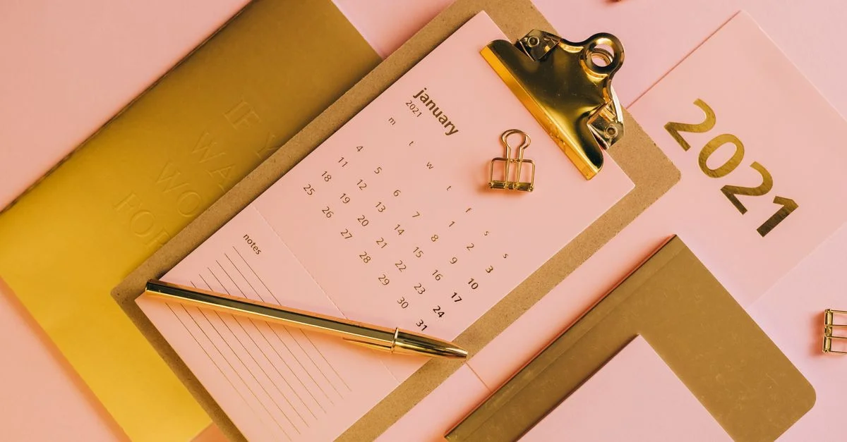 Arrangement élégant de papeterie rose et dorée avec calendrier et tableau blanc pour un look de bureau moderne.