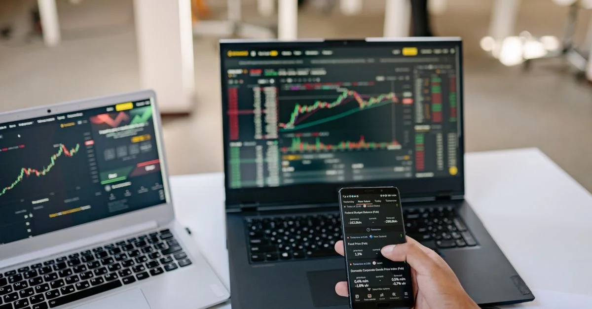 Un professionnel suit les tendances du marché boursier en utilisant deux ordinateurs portables et un smartphone, mettant en avant des outils de finance numérique.