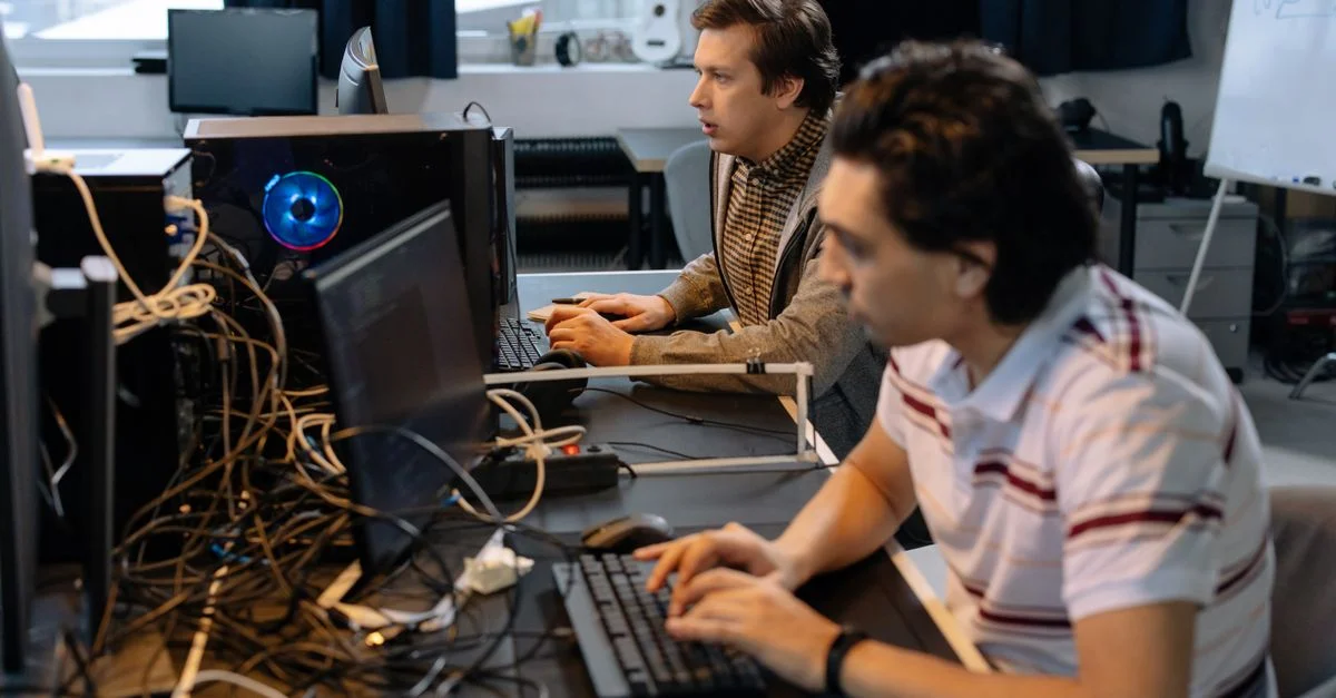 Des programmeurs masculins travaillant sur des ordinateurs dans un cadre de bureau moderne, mettant en avant le travail d'équipe et la technologie.