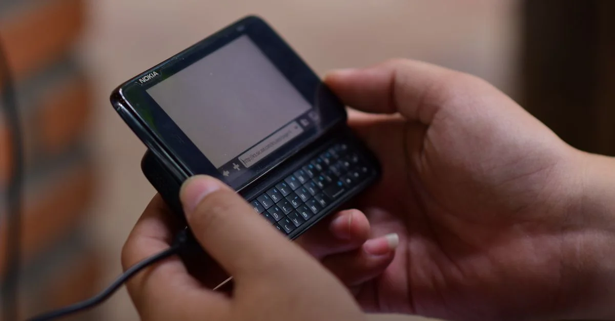 Mains manipulant un téléphone portable vintage à clavier coulissant, à l'intérieur. Gros plan.