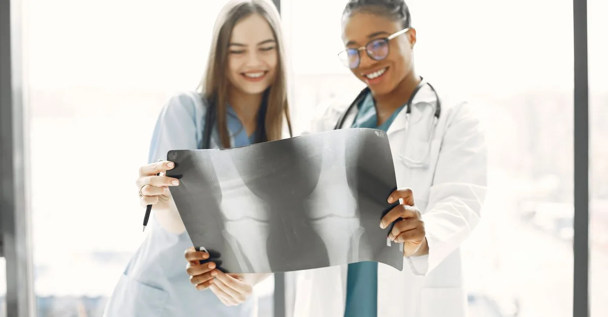 Deux professionnels de la santé souriants analysant une radiographie dans une salle d'hôpital bien éclairée.