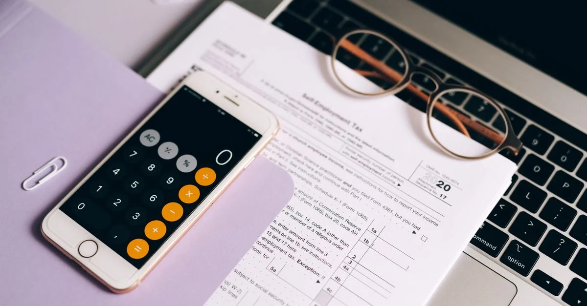 Un smartphone avec une application de calculatrice sur des documents fiscaux à côté d'un ordinateur portable, mettant en avant la comptabilité moderne.