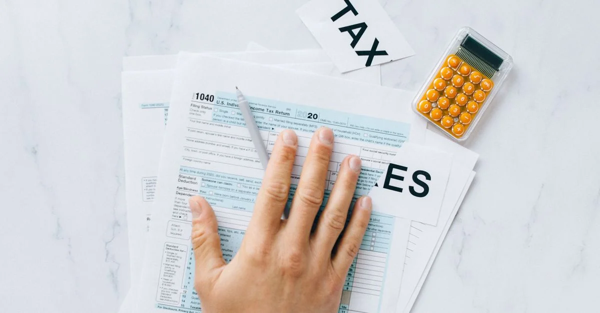 Gros plan d'une main sur le formulaire fiscal 1040 avec une calculatrice sur un bureau.