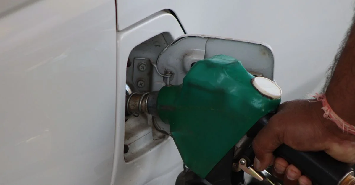 Gros plan d'une main remplissant le réservoir d'essence d'une voiture dans une station équipée d'une buse de carburant verte.