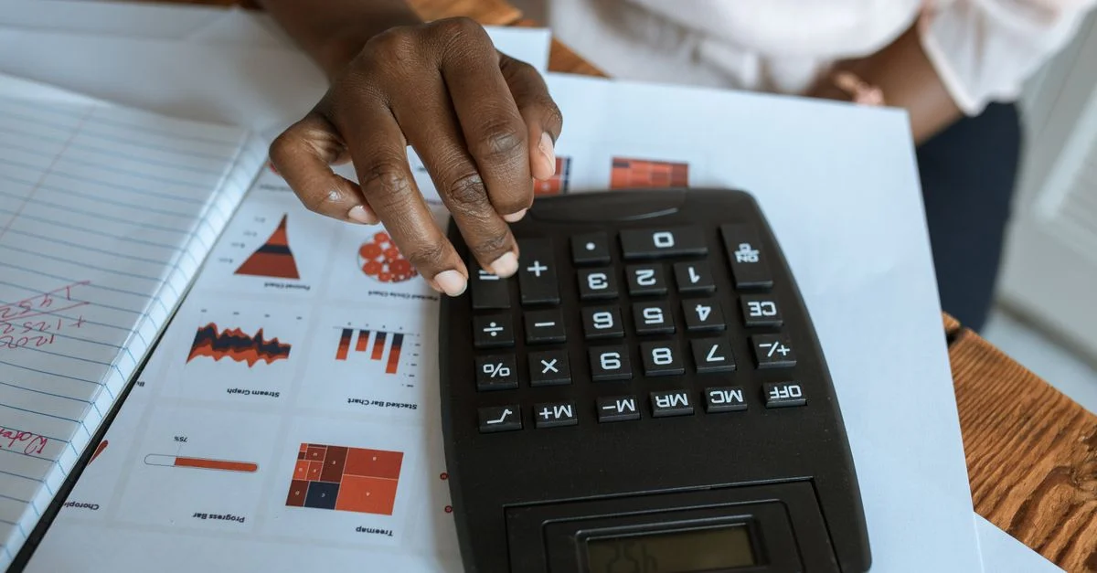 Personne utilisant une calculatrice sur un bureau avec des graphiques et des tableaux financiers, idéal pour des thèmes d'affaires et de finance.