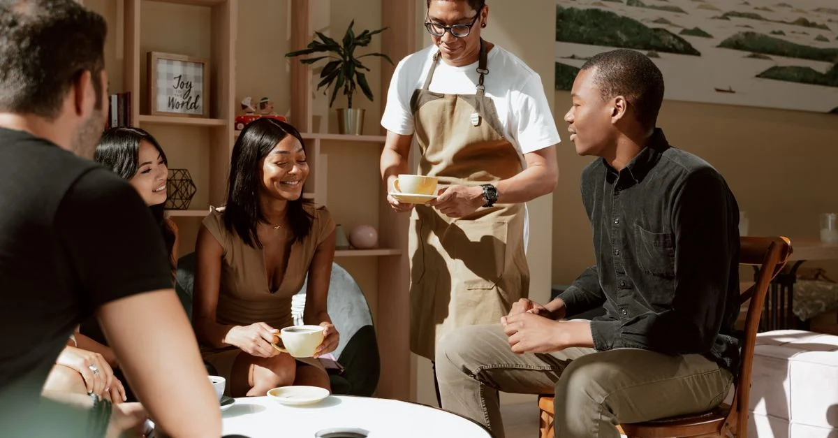 Un groupe d'amis dégustant un café servi par un serveur dans un cadre de café confortable.
