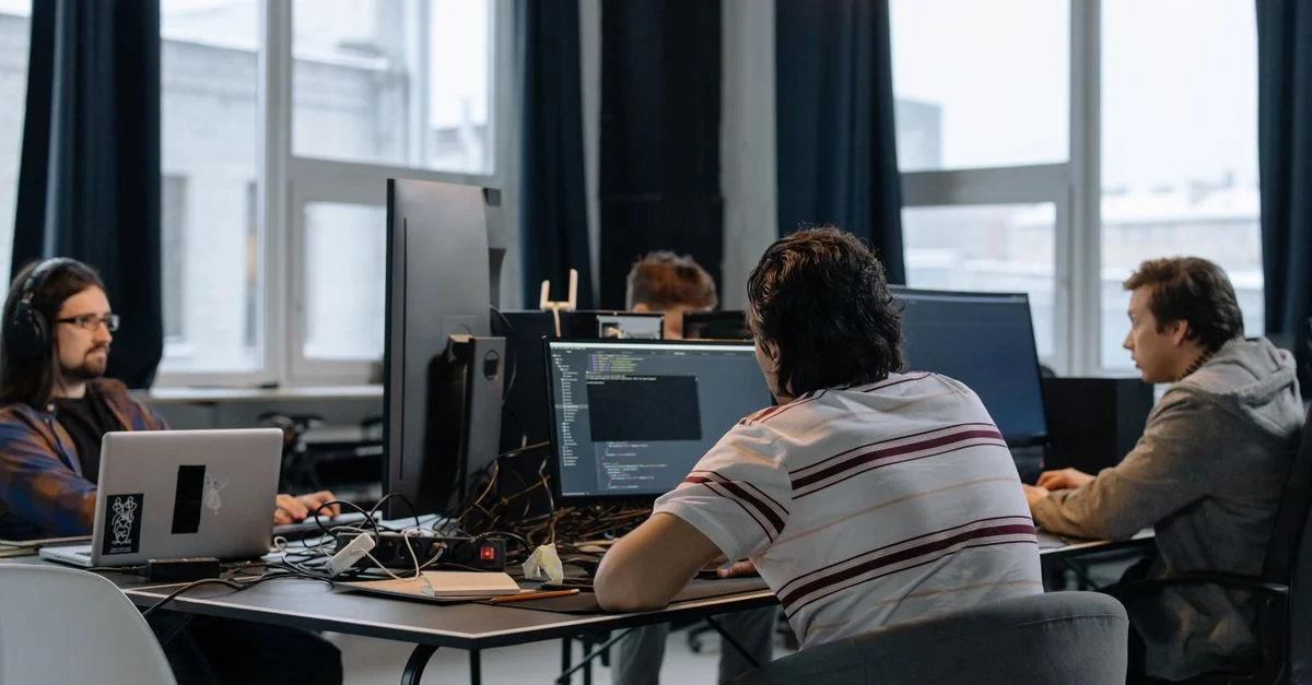 Équipe de développeurs travaillant ensemble sur des ordinateurs dans un bureau tech moderne.