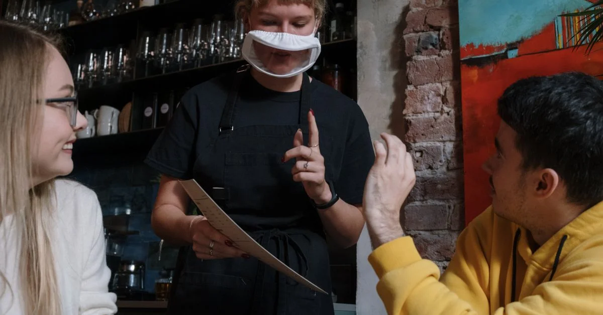 Une serveuse utilisant la langue des signes pour prendre une commande de clients dans un café moderne.
