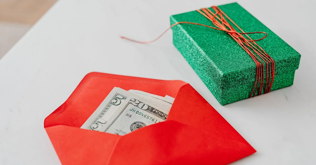 Une enveloppe rouge festive avec des billets en dollars américains à côté d'une boîte cadeau verte, parfaite pour des occasions spéciales.