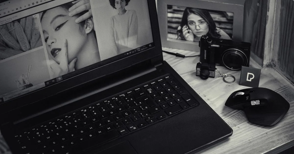 Un espace de travail au thème noir et blanc comportant un ordinateur portable, un appareil photo et une photo encadrée sur un bureau.