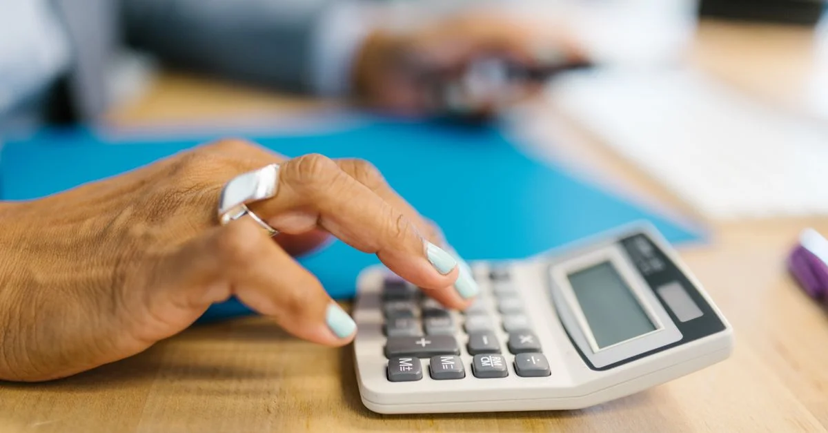 Main manucurée utilisant une calculatrice sur un bureau avec un dossier bleu, faible profondeur de champ.