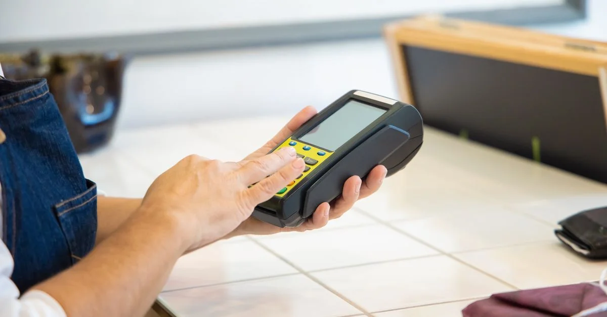 Gros plan sur des mains utilisant un terminal de paiement dans un environnement de vente au détail, mettant l'accent sur le paiement numérique.