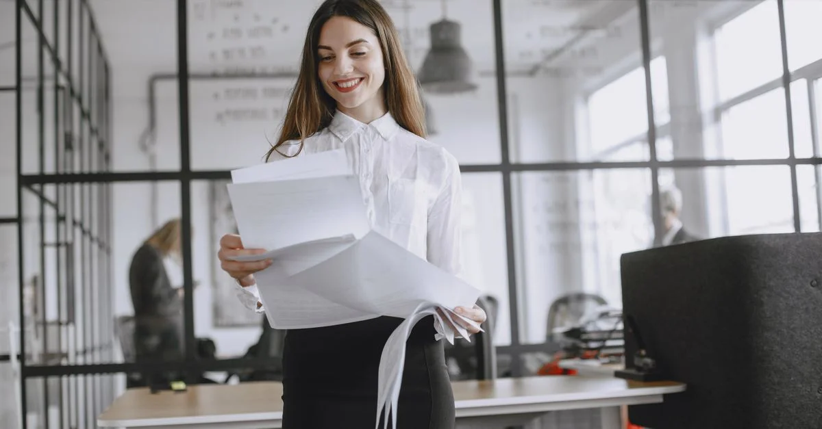 Femme confiante aux longs cheveux examinant des documents à son bureau moderne.