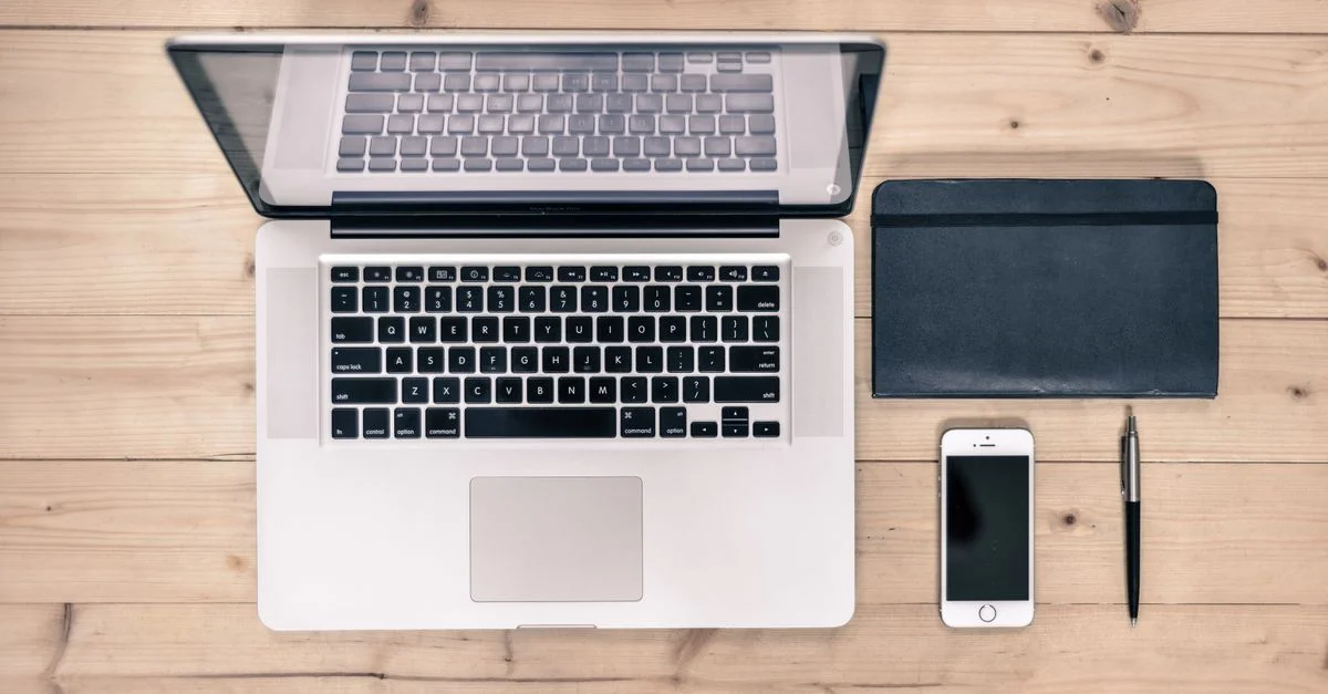 Vue de dessus d'un espace de travail soigné avec un ordinateur portable, un smartphone, un carnet et un stylo sur un bureau en bois.