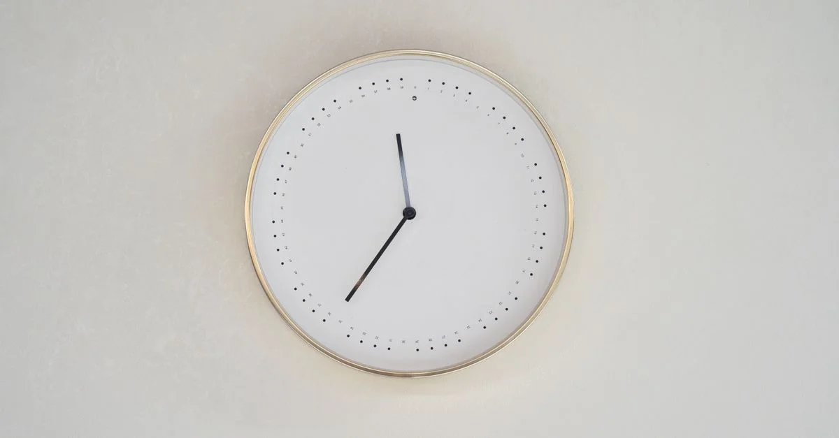 Une horloge murale au design minimaliste avec un bord doré et sans chiffres sur un fond neutre.