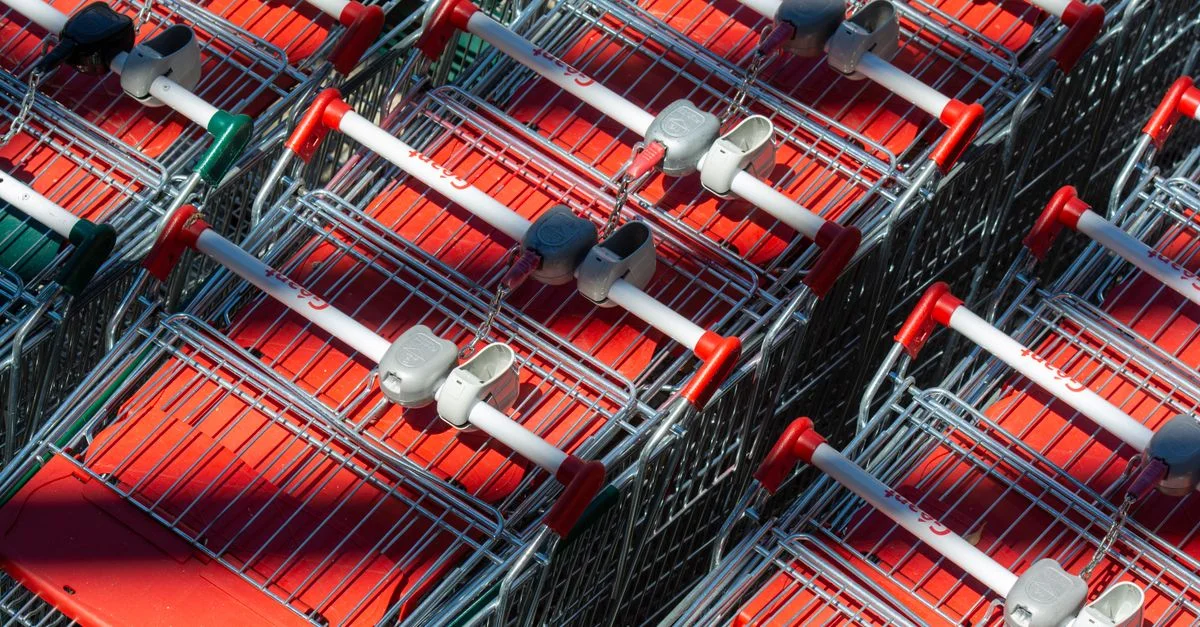 Chariots de courses soigneusement disposés projetant des ombres sous un soleil éclatant, mettant en valeur l'extérieur d'un supermarché.